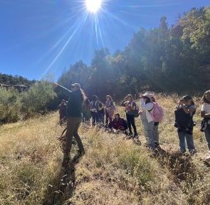 Educator teaching students outside in field with trees around on sunny day