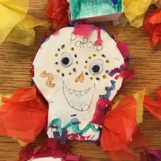 Smiling face with googly eyes on white skull-shaped paper. Colorful tissue paper glued around.