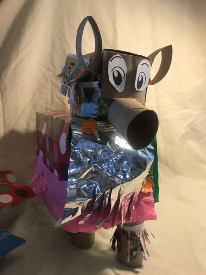 Animal made of boxes, toilet paper rolls, with big ears, big printed eyes, and body covered in cellophane, wrapping paper, and tissue paper.