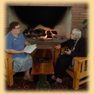 Two people talking and holding papers in front of fireplace.