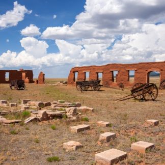 Old fort wall, wagons in field around wall, stone bricks in foreground. Partly cloudy sky.