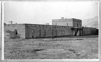 Black and white old photo of fort. Long low building with one section on second story. Many windows.