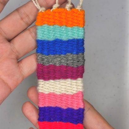Small strip of woven rug with bright stripes, being held by two hands.