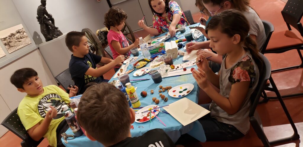 Group of kids painting at a table filled with paints, brushes, and other craft supplies